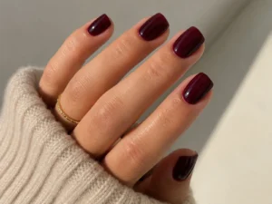 Main avec manucure bordeaux sur ongles courts